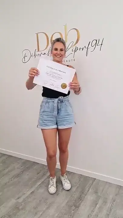 Une stagiaire en short en jean présente son attestation devant le lettrage mural du centre.