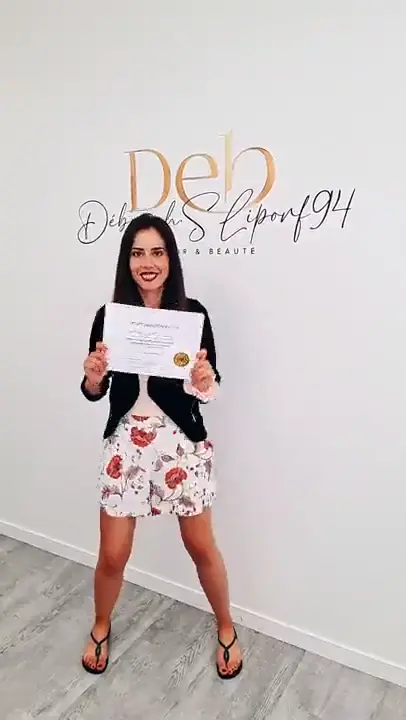 Une stagiaire en jupe fleurie tient son attestation devant le lettrage doré.