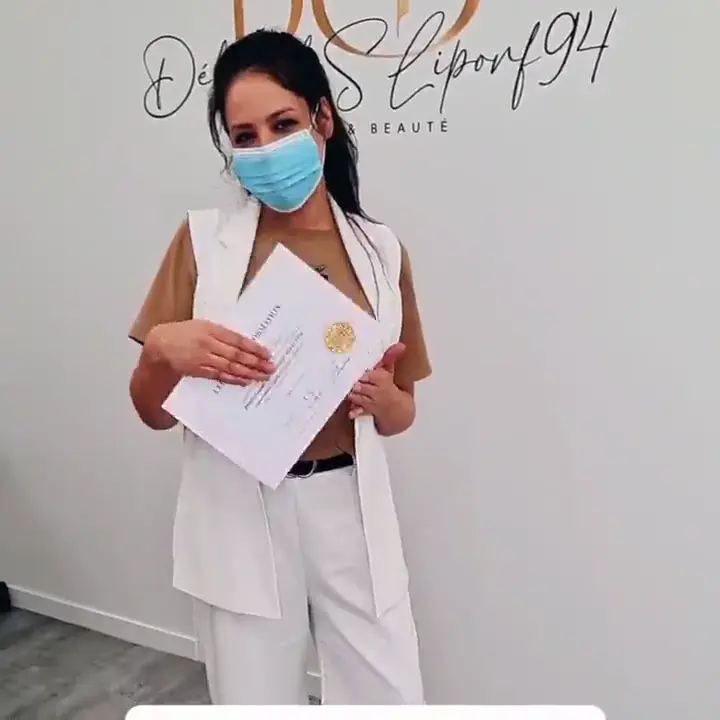 Une stagiaire en ensemble blanc, masque sur le visage, présente son attestation.