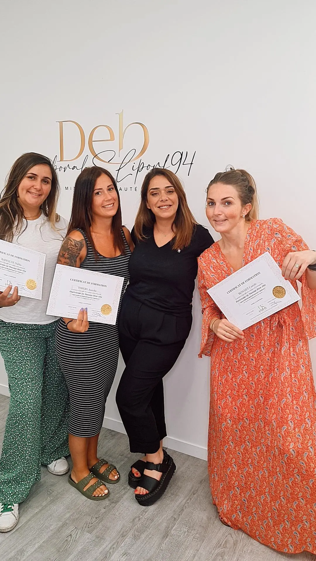 Quatre stagiaires d’une même promotion présentent leurs attestations côte à côte devant le lettrage mural du centre.