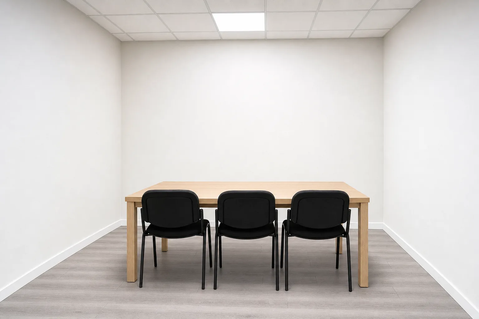 Salle de formation vide : une table claire, trois chaises, un mur uni sous plafonnier.