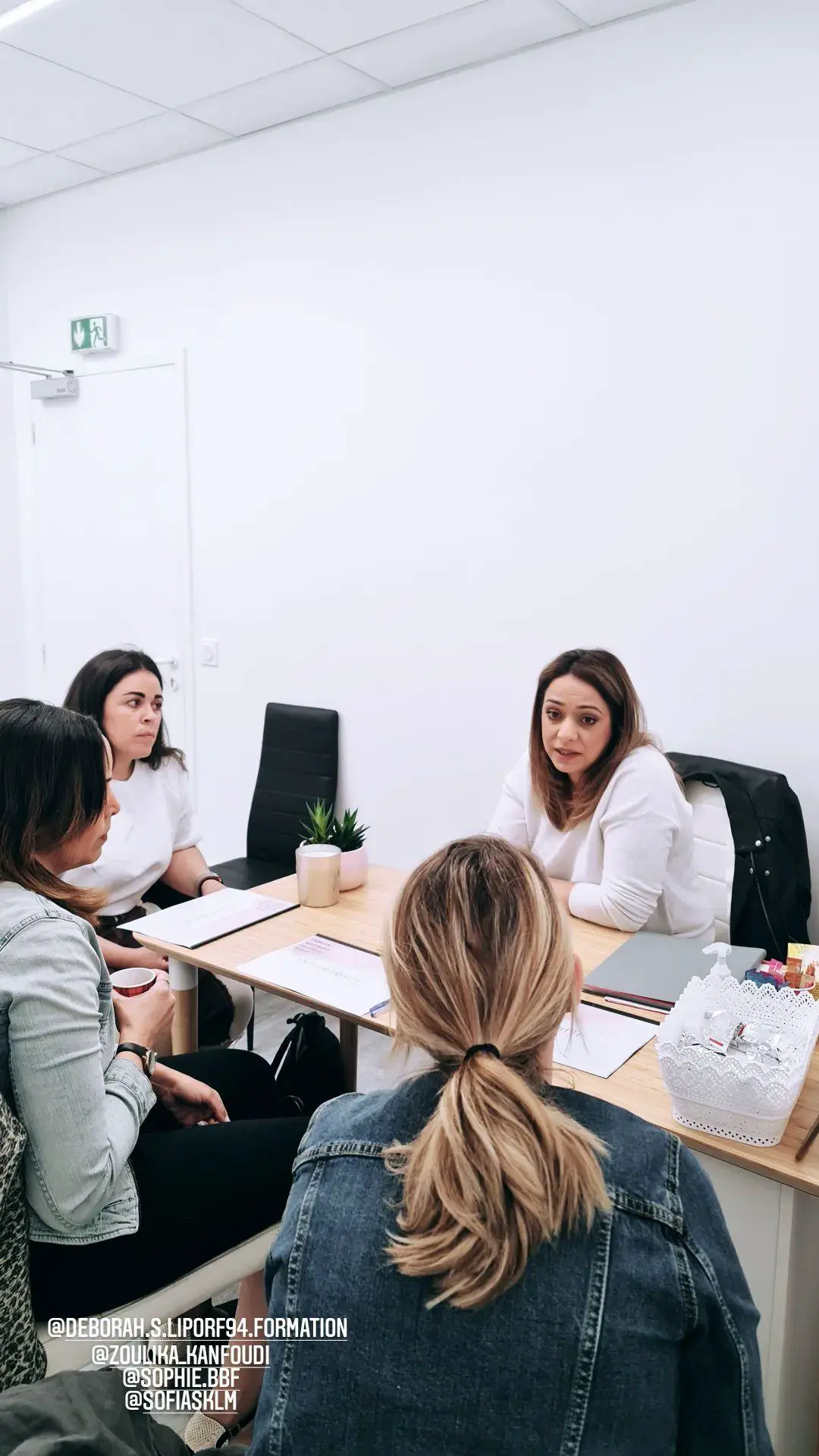 Trois personnes autour d’une table de travail, ordinateurs ouverts et dossiers étalés, dans la salle du centre.
